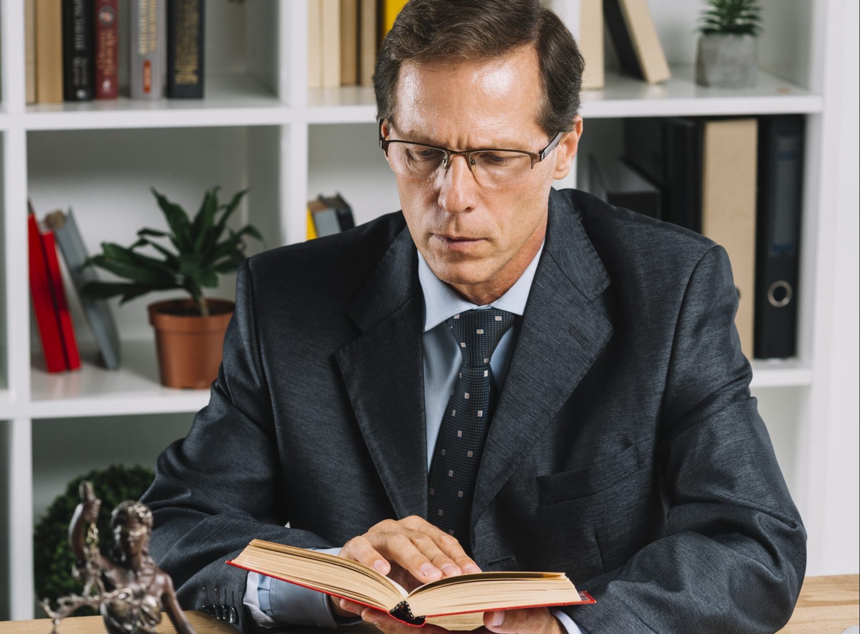 mature-male-lawyer-reading-book-with-gavel-justice-statue-wooden-table